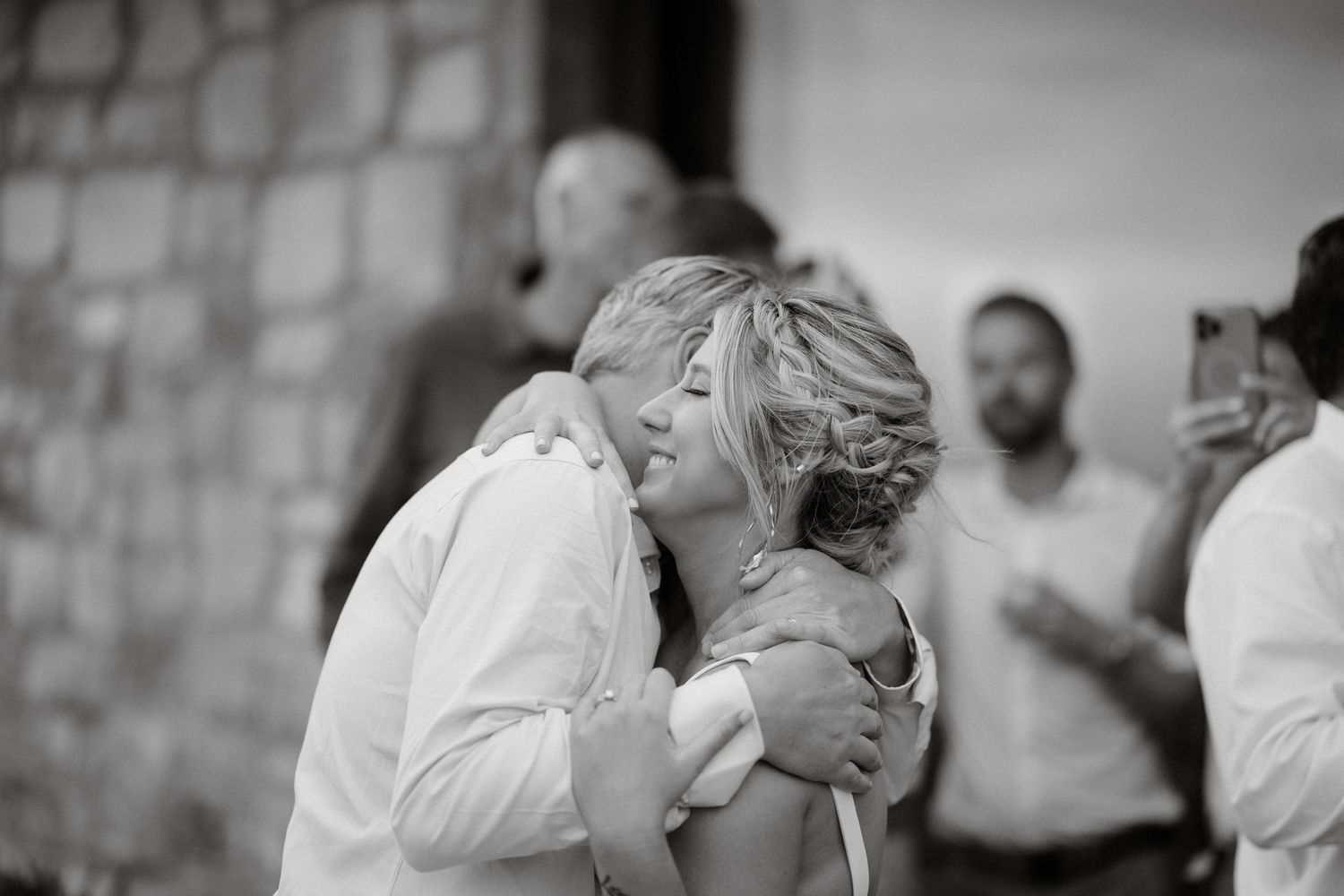 A tender romantic embrace captured in black and white at a stone wall venue during a special occasion.