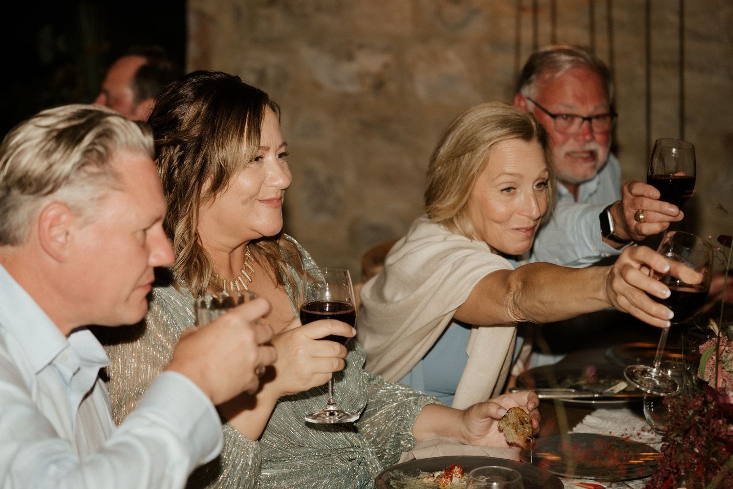 Wedding guests toasting with wine glasses during intimate dinner reception.