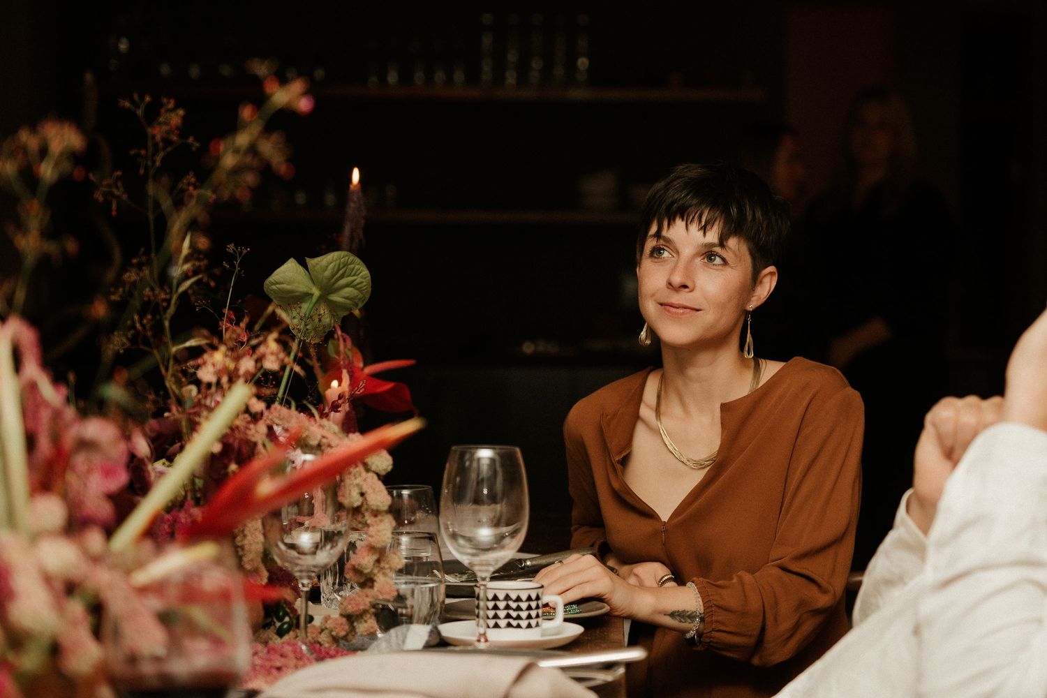A guest enjoys a candlelit dinner at an elegantly set table with floral arrangements.