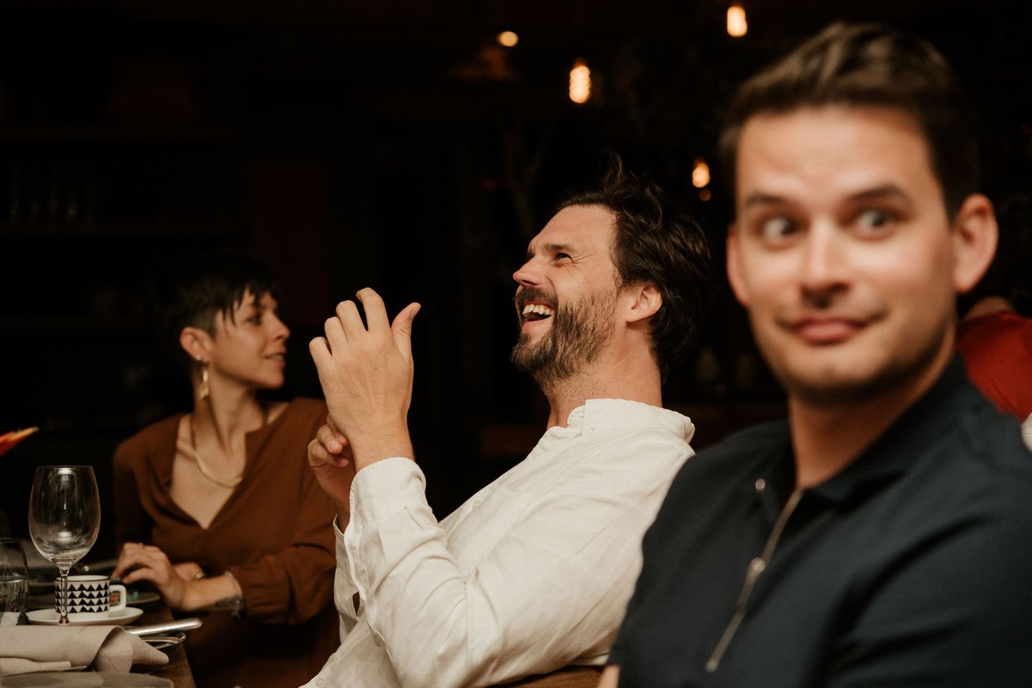 Group enjoying laughter and conversation at dimly lit dinner gathering.