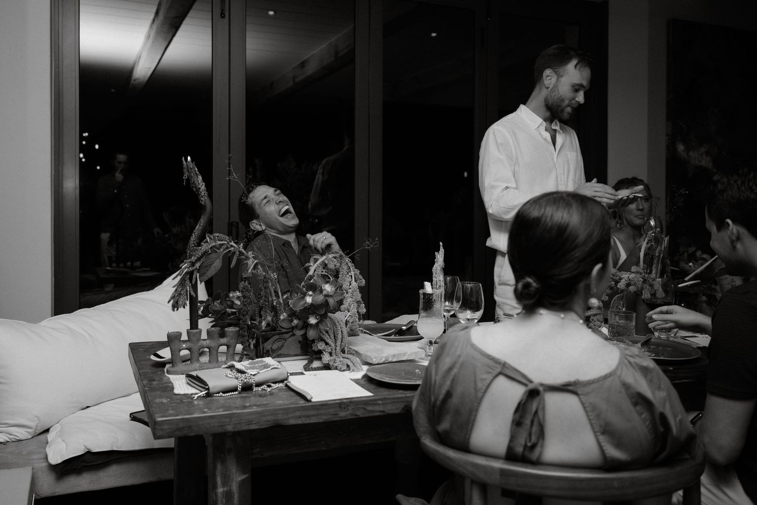 Black and white photo of intimate dinner gathering with table decorations and candlelight.