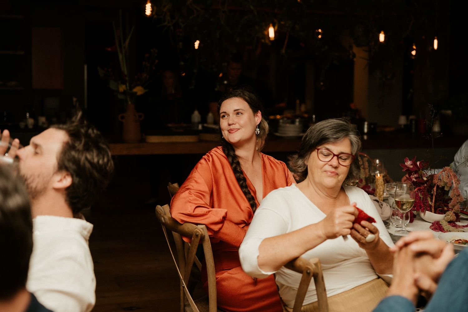 Candid shot of dinner guests enjoying conversation at dimly lit restaurant table.