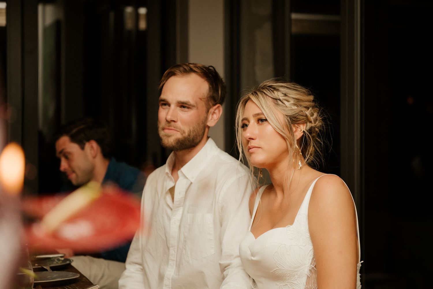 Couple in white attire seated together at an elegant dinner party.