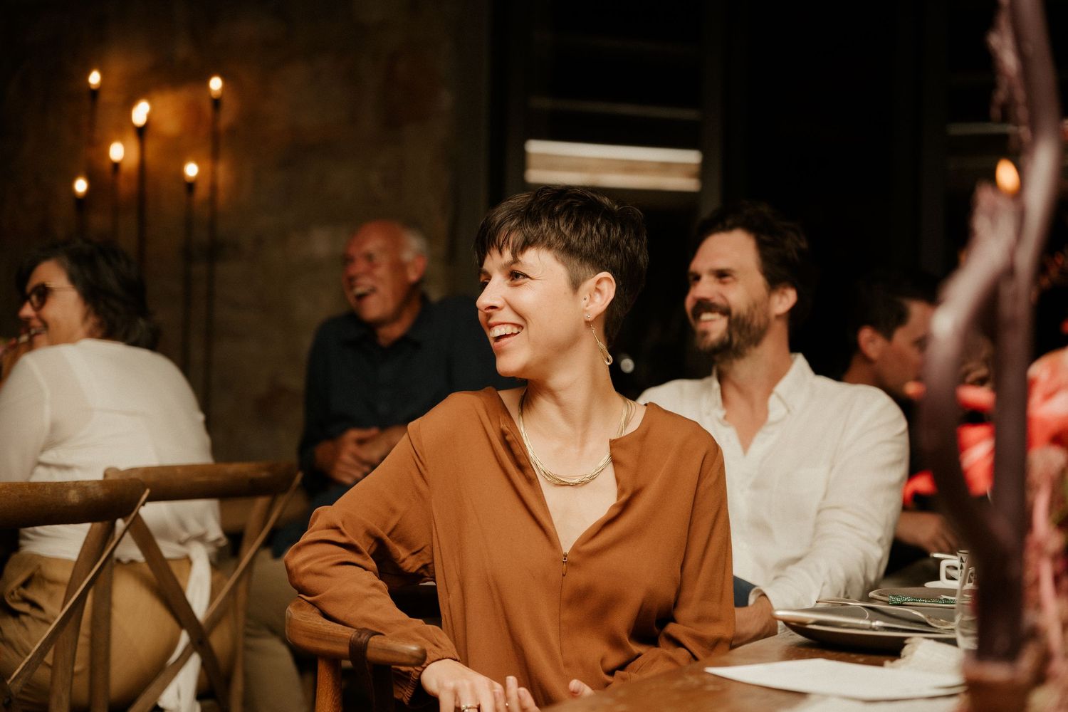 People enjoying themselves at a candlelit dinner gathering with warm ambient lighting.
