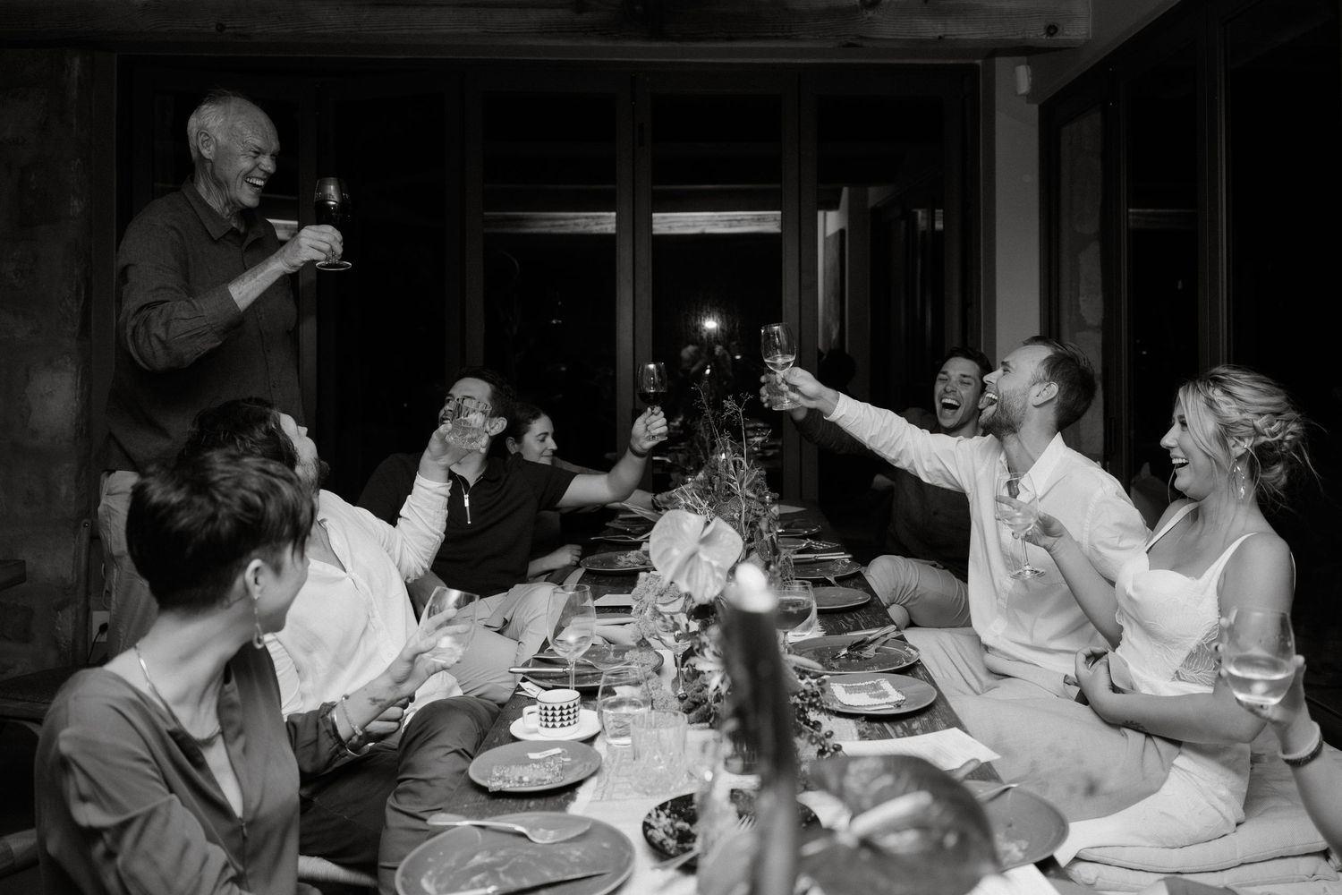 Black and white photo of dinner guests raising their glasses in a celebratory toast.