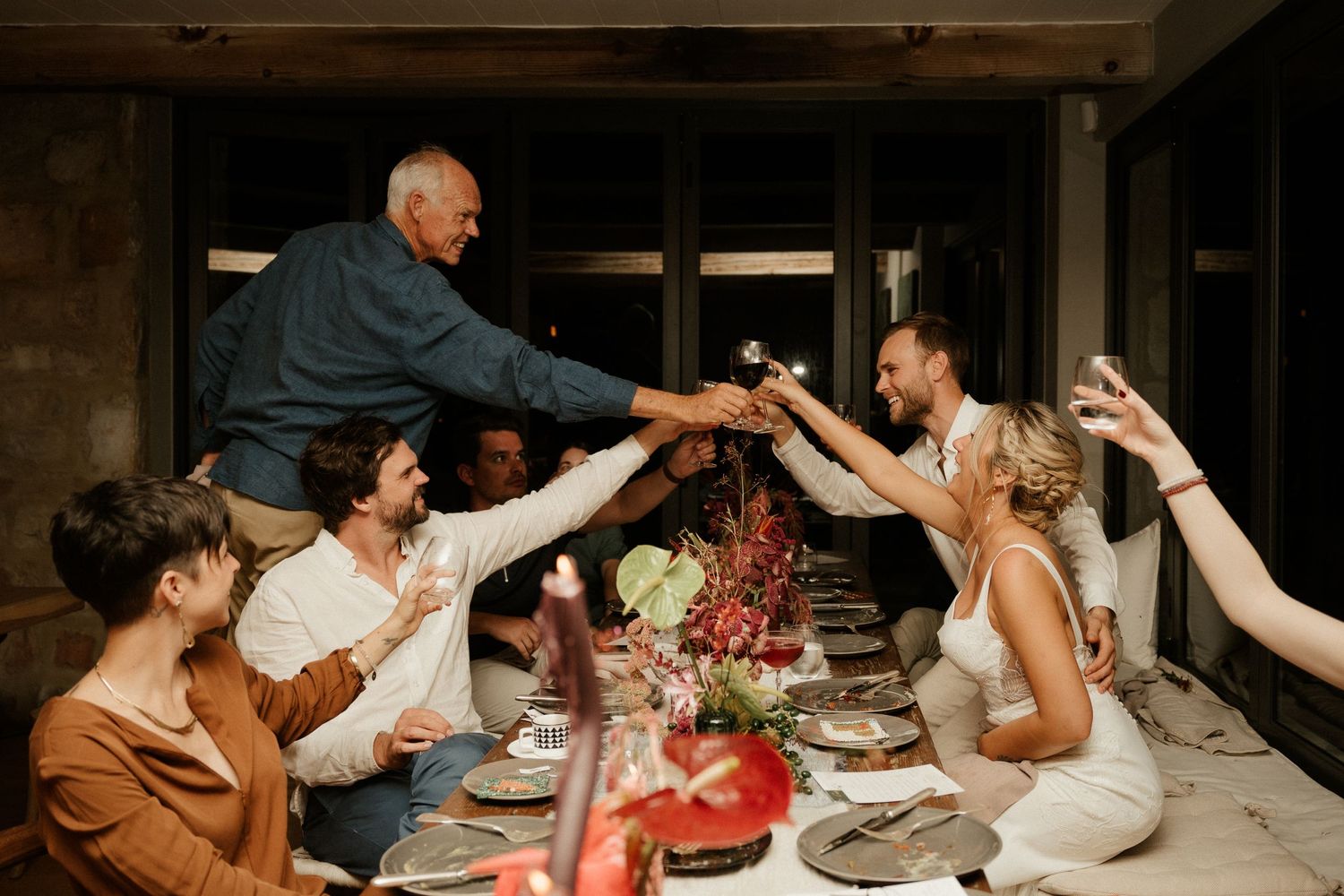 A lively celebration dinner party with guests toasting and raising glasses across a decorated table.