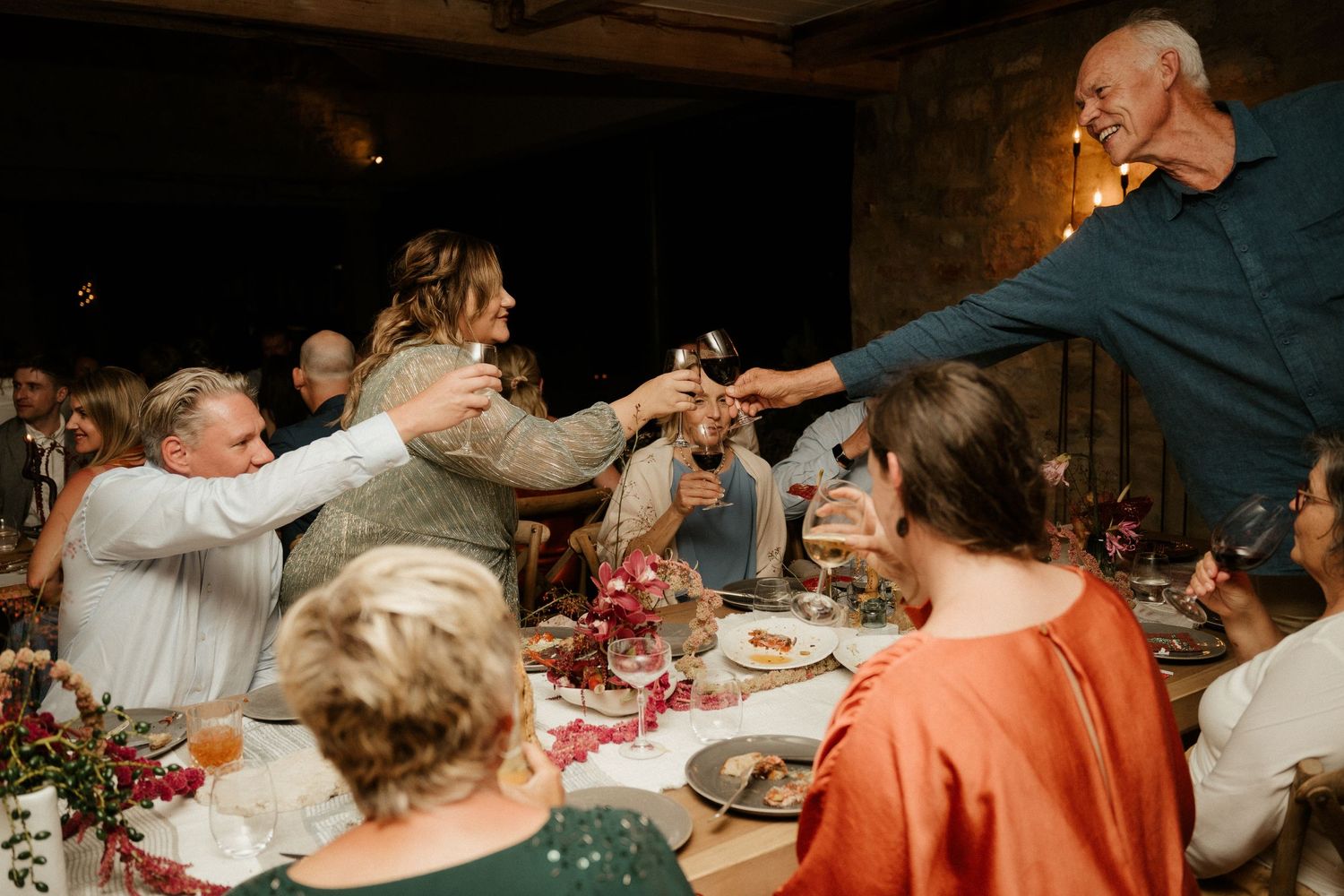 Dinner guests raise their glasses for a celebratory toast at an intimate gathering with warm lighting and table decorations.