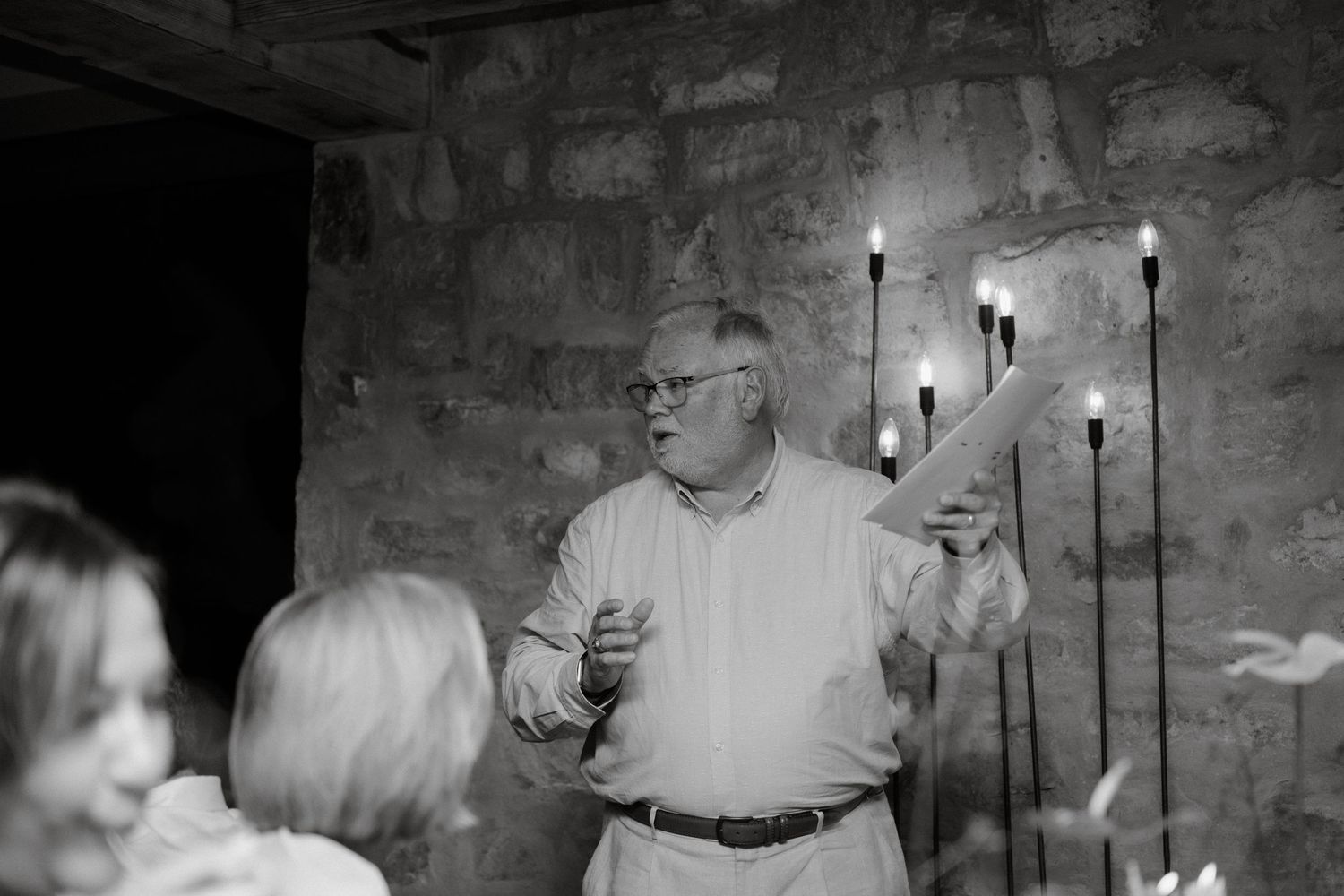 A speaker in white dress shirt gestures while giving a speech at a stone-walled venue.