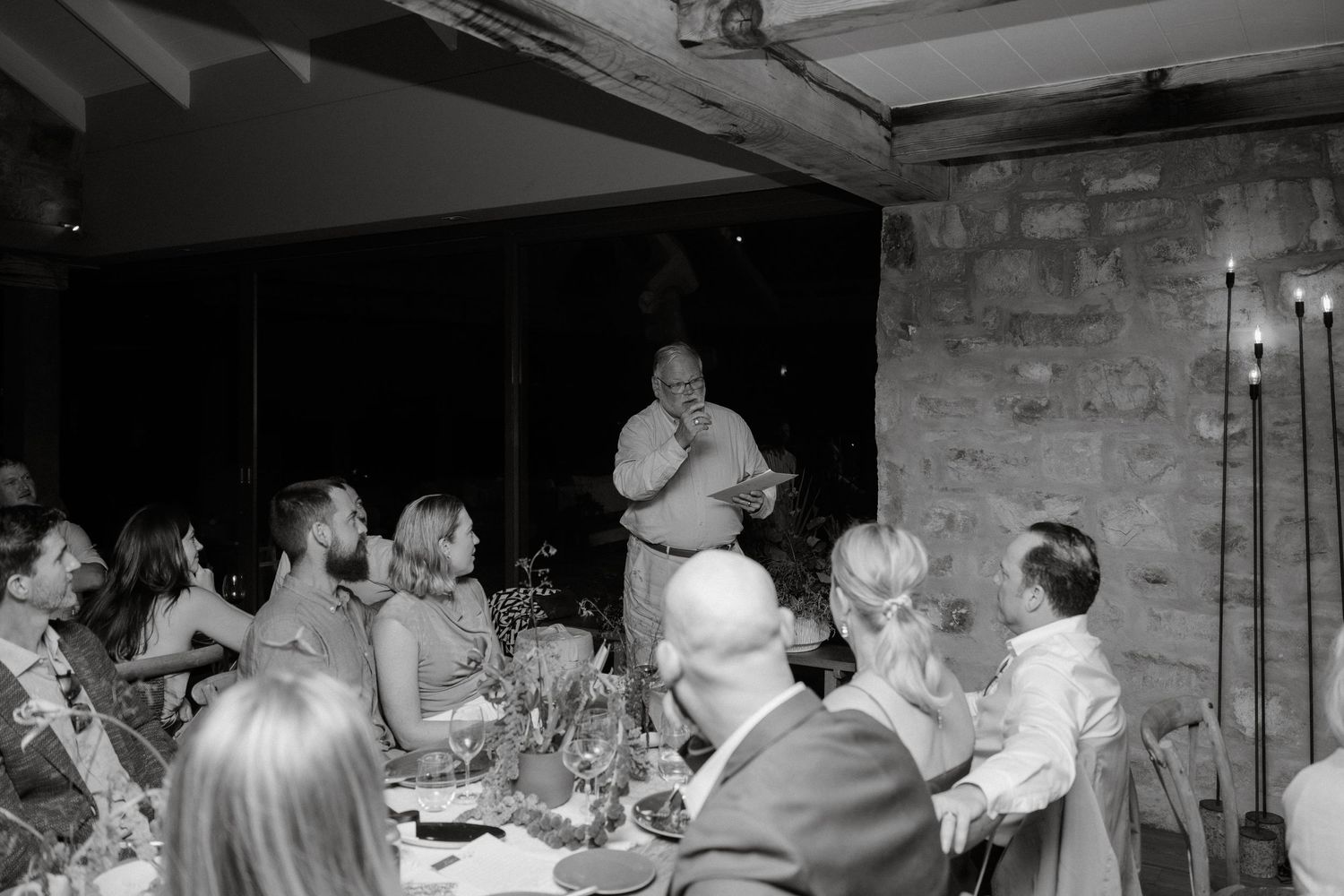 Black and white photo of dinner guests listening attentively to someone speaking at an elegant dinner party.