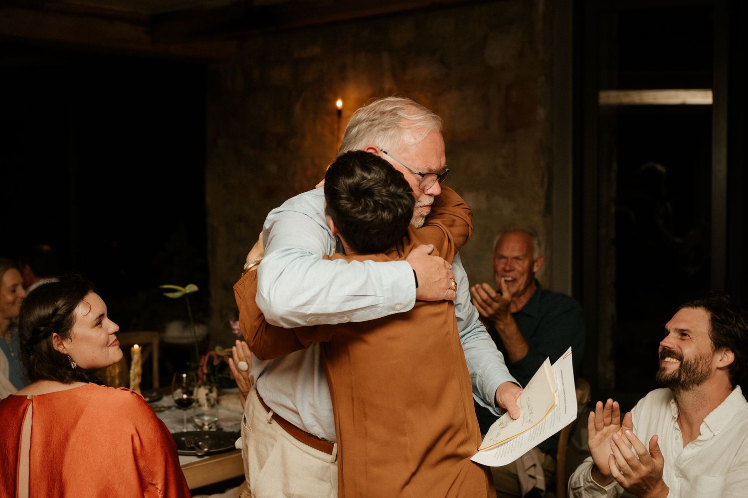 Emotional embrace captured during celebration dinner with guests applauding.