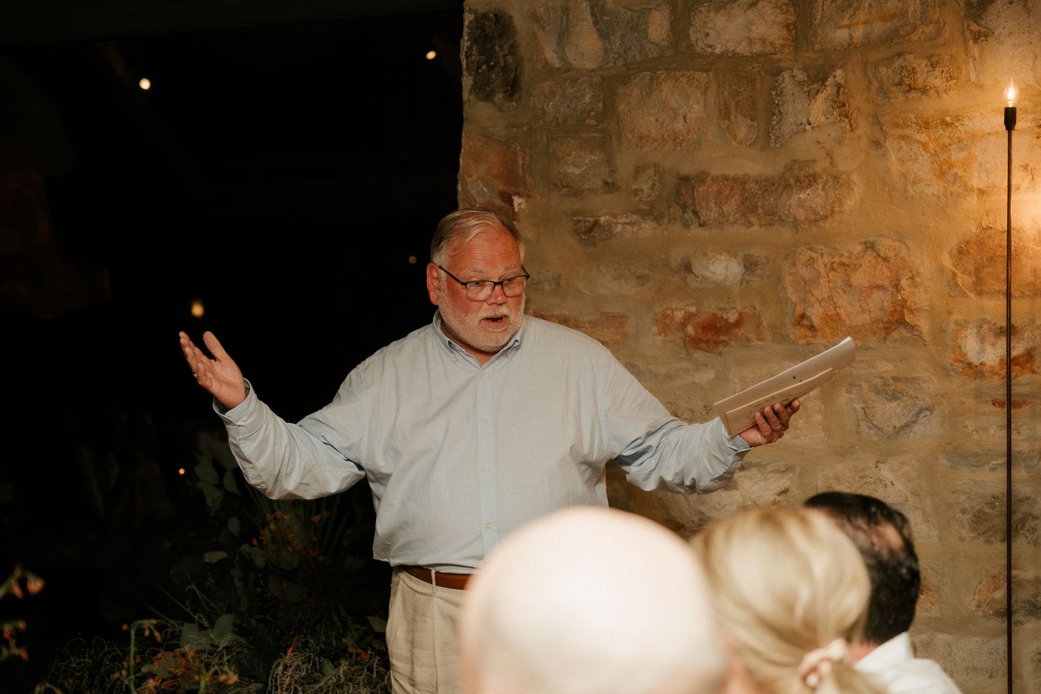 A speaker gestures enthusiastically while addressing an audience in a rustic stone venue.