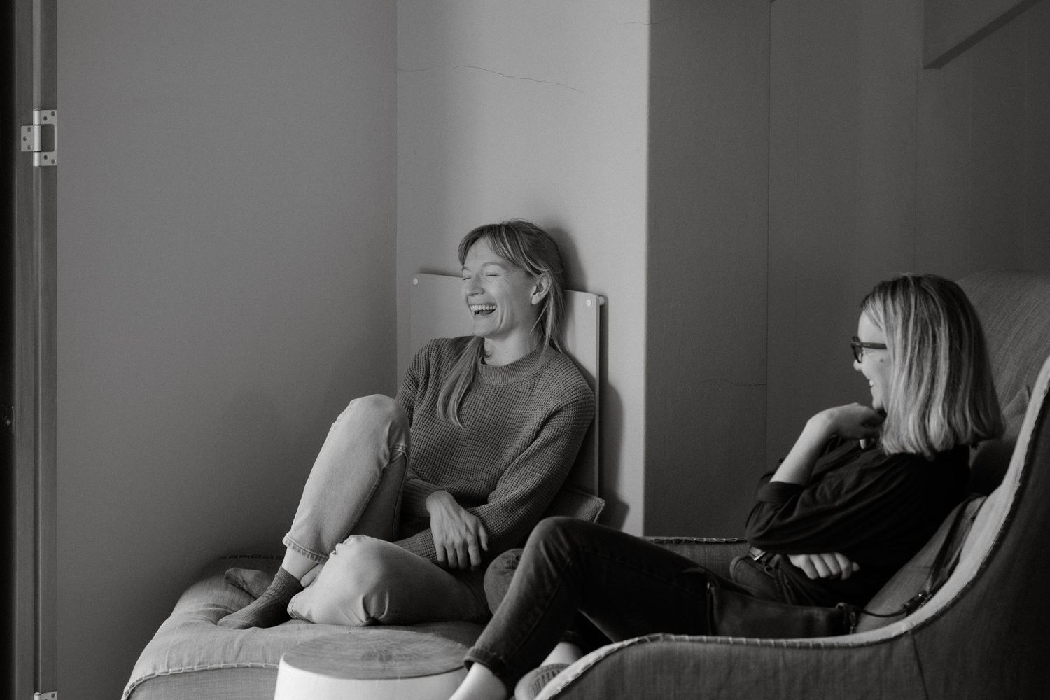 Two people relaxing and sharing a laugh while lounging in chairs by a window.