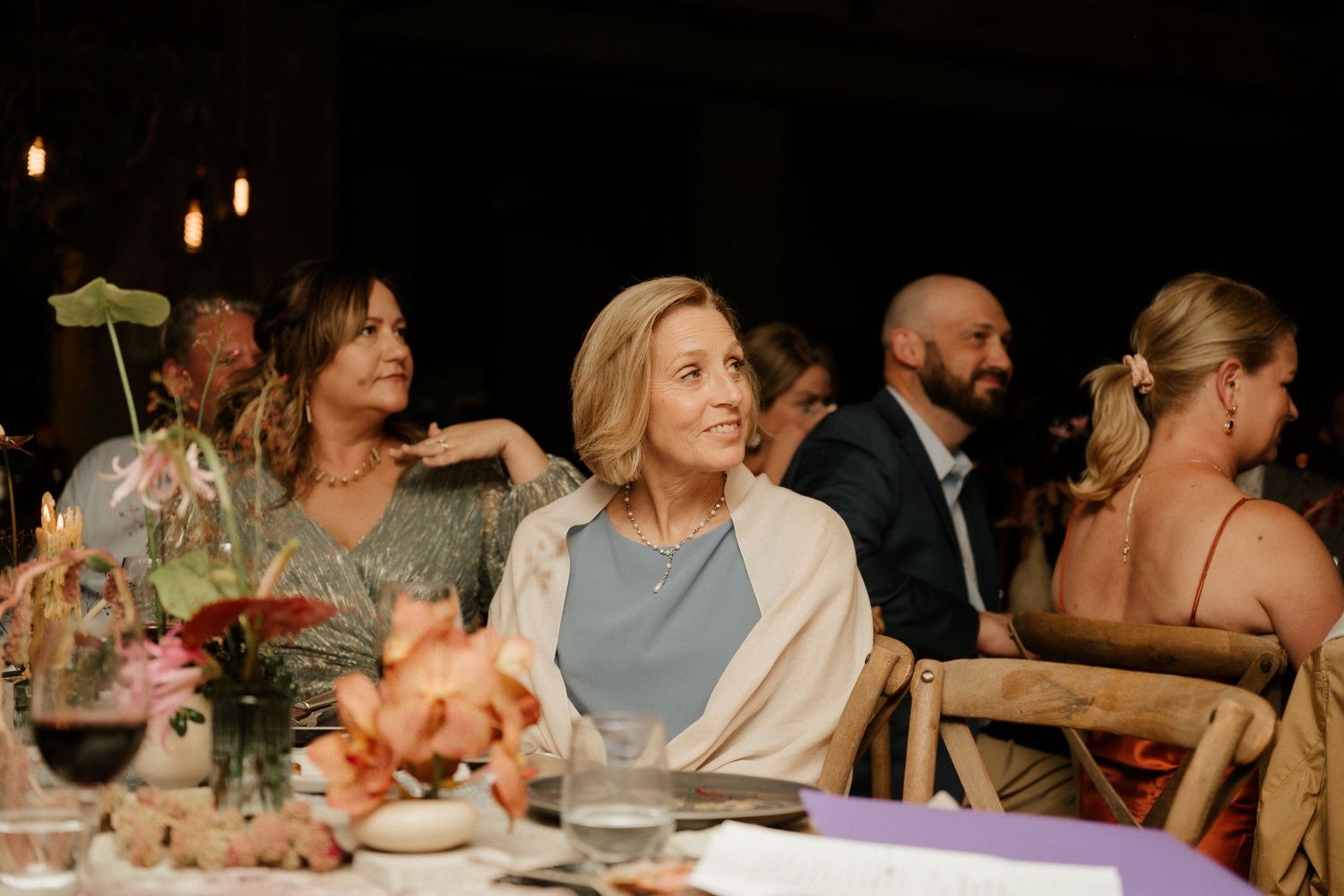 Wedding guests enjoy a candlelit dinner at an elegantly decorated reception table with floral centerpieces.