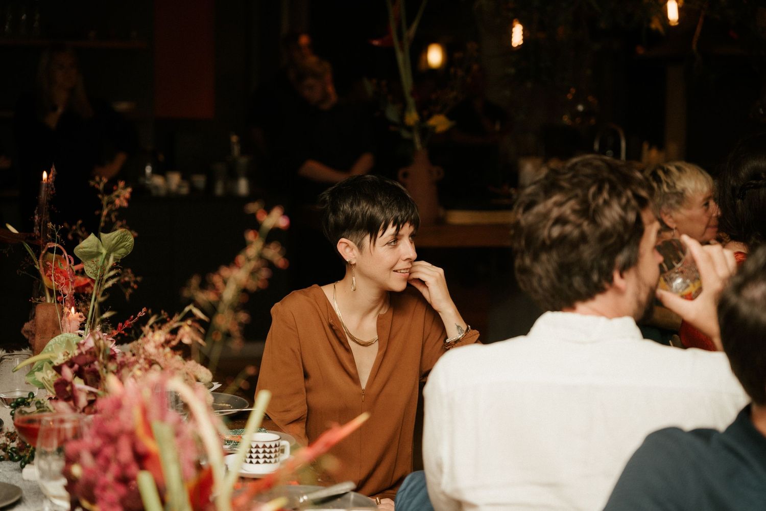 Dinner guests engage in conversation at a beautifully decorated table with pink floral arrangements.