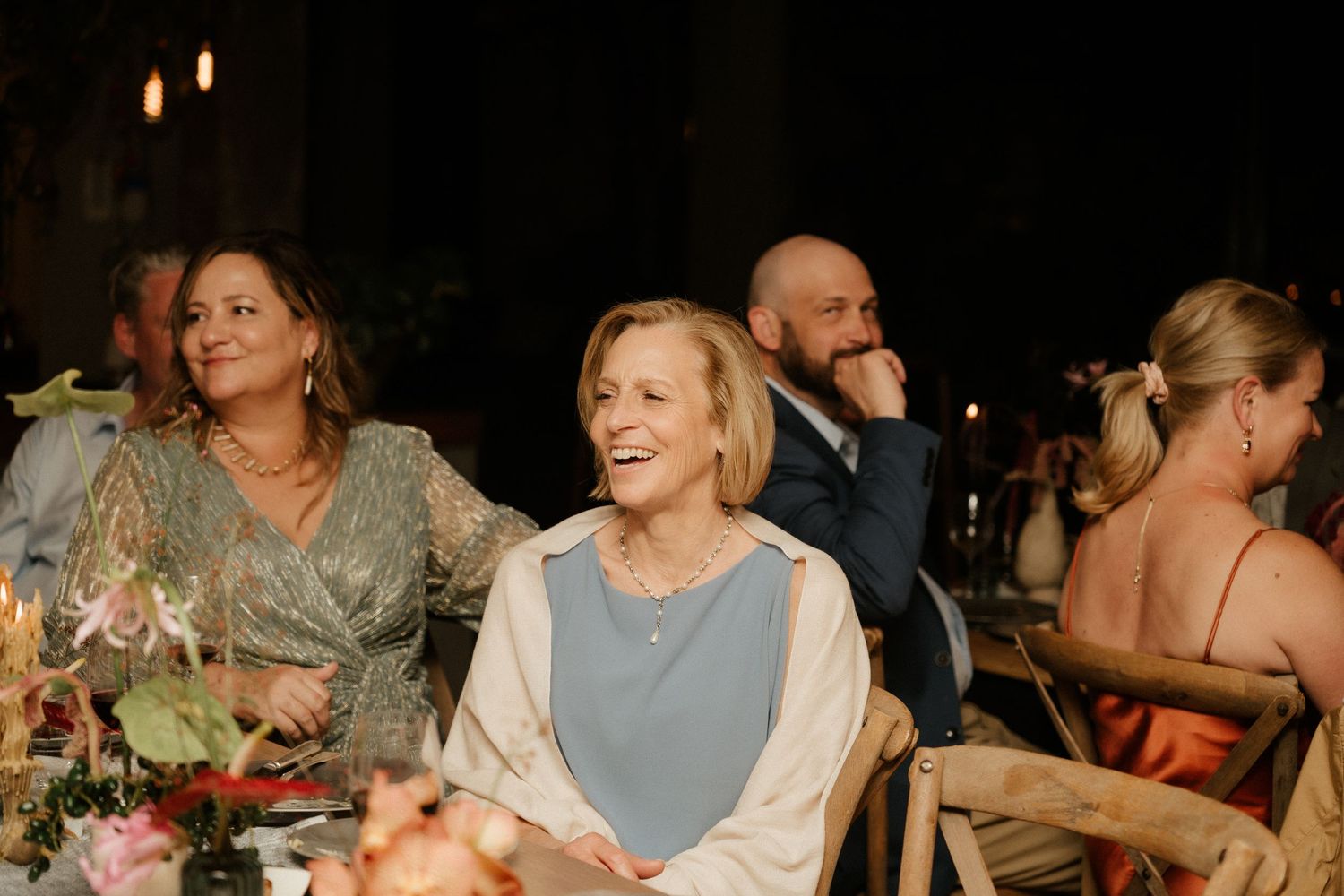 Guests seated at an elegant dinner table with floral centerpieces and candlelight.