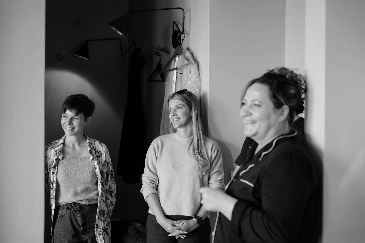 Three people laughing and chatting together in a casual black and white interior setting.
