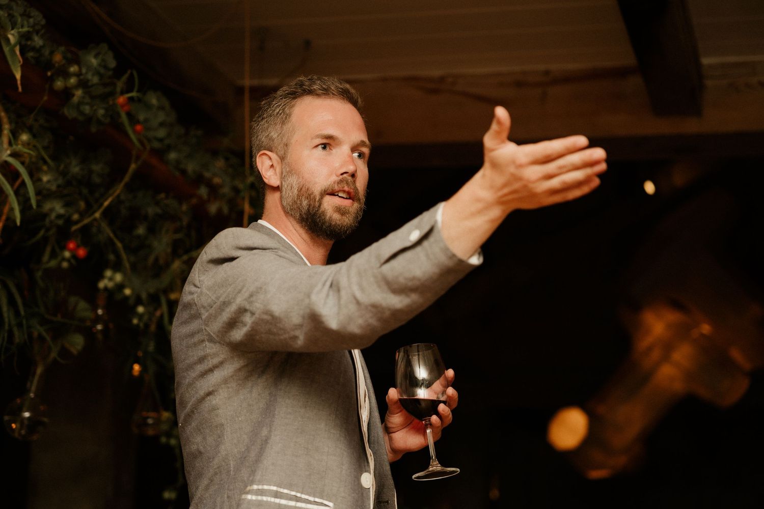 Speaker in grey suit gesturing animatedly during evening celebration speech.