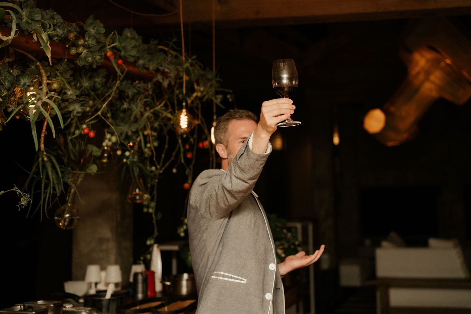 Person in gray attire raises a toast with a wine glass under decorative hanging plants.