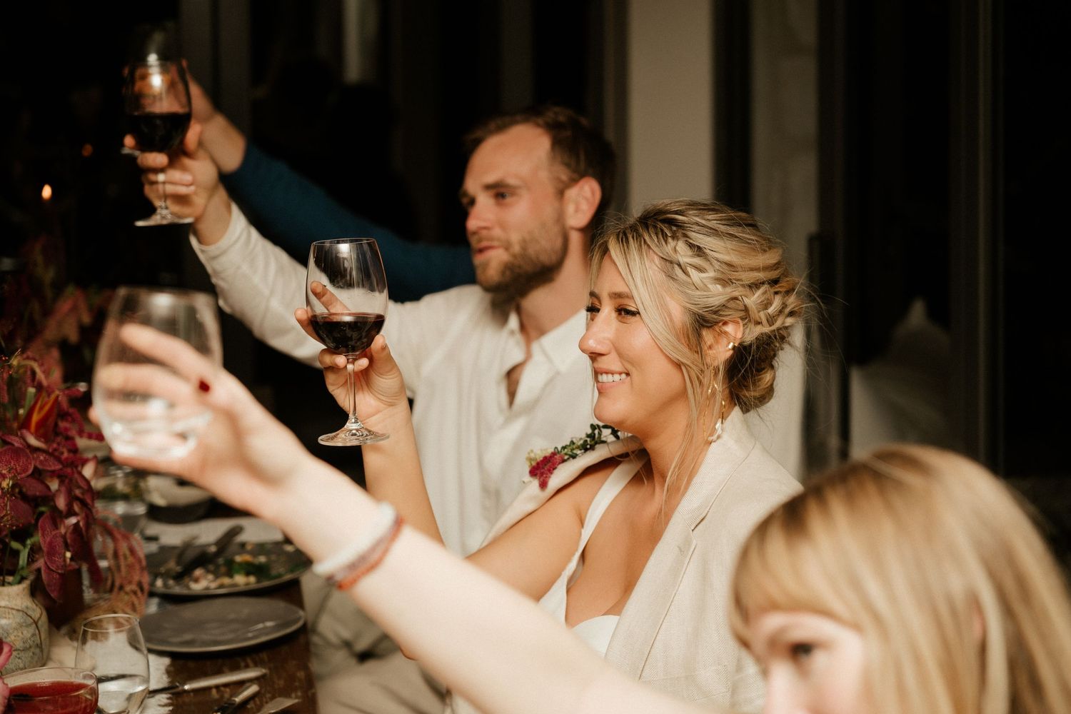 Wedding reception guests raising wine glasses in a celebratory toast at dinner.