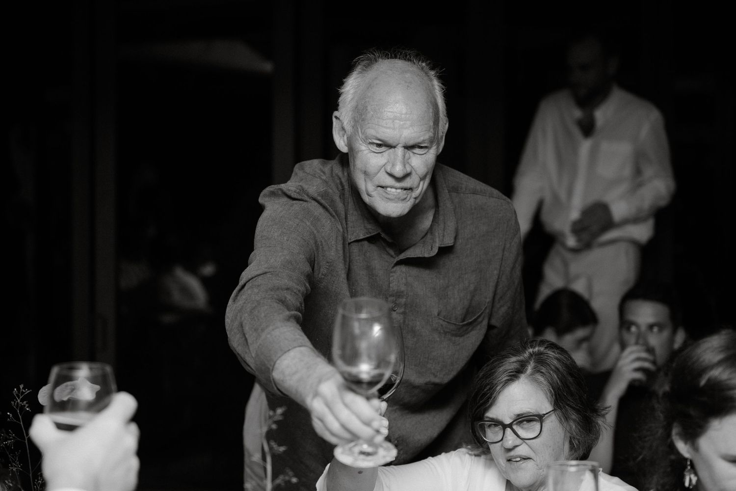 A black and white candid photo of guests interacting at an elegant dinner party.