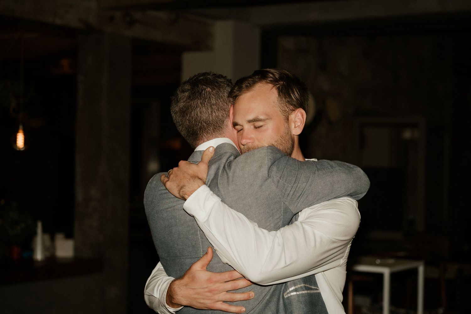 Two people share an emotional embrace in a dimly lit indoor setting.
