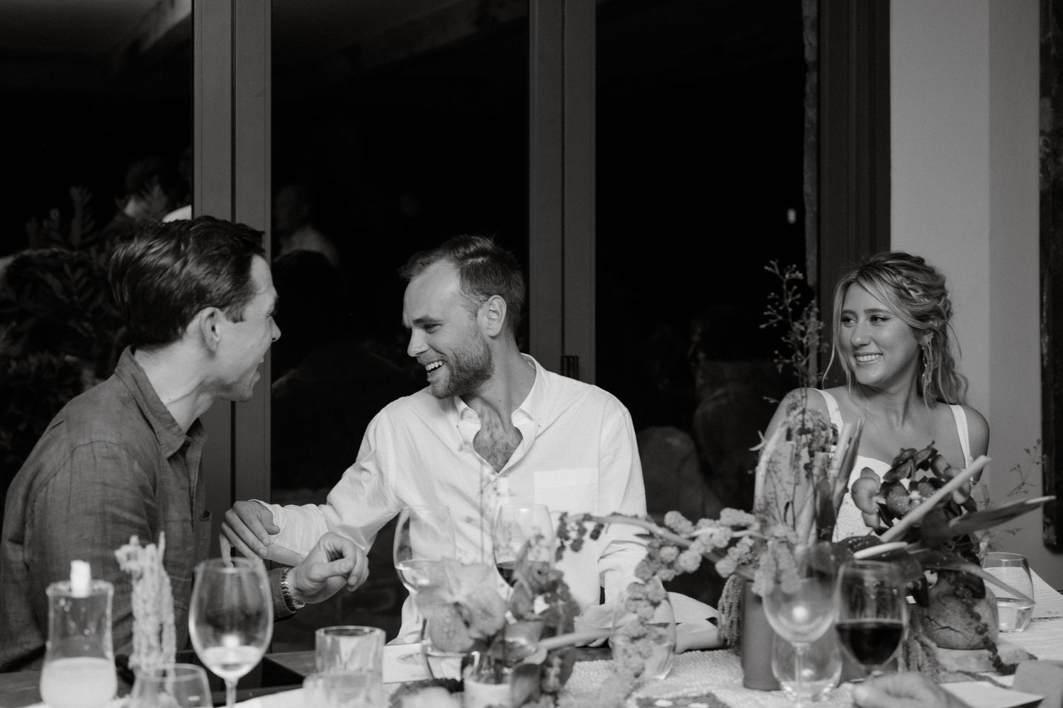 Black and white photo of dinner guests engaged in conversation at an elegant table setting.