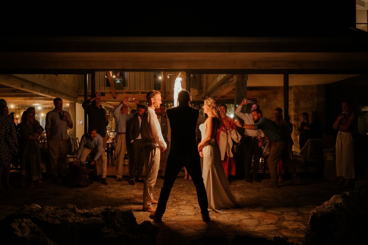 Silhouetted figures dance in dramatic lighting at an evening wedding reception.