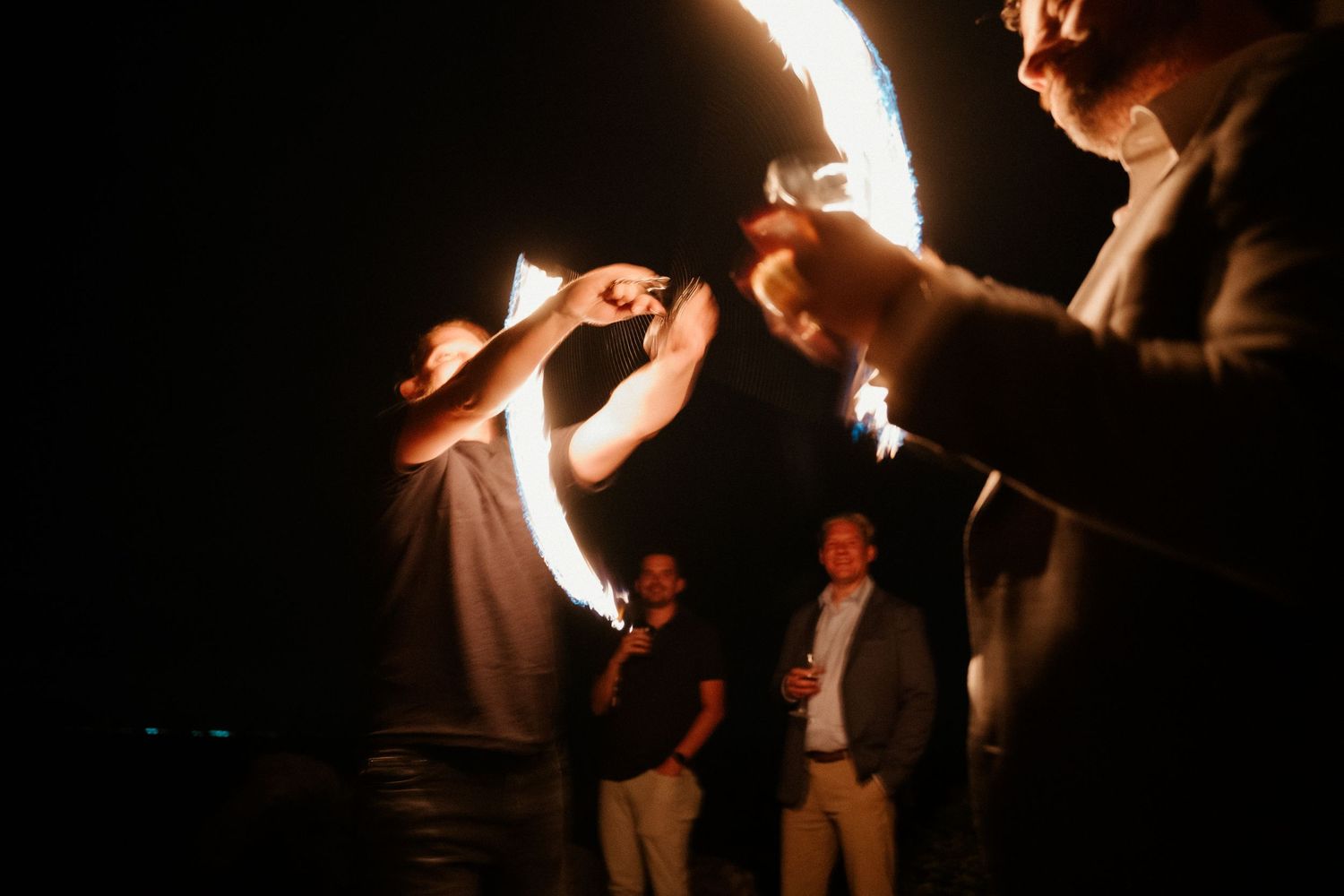 People holding sparklers create dramatic light trails in the darkness during an evening celebration.