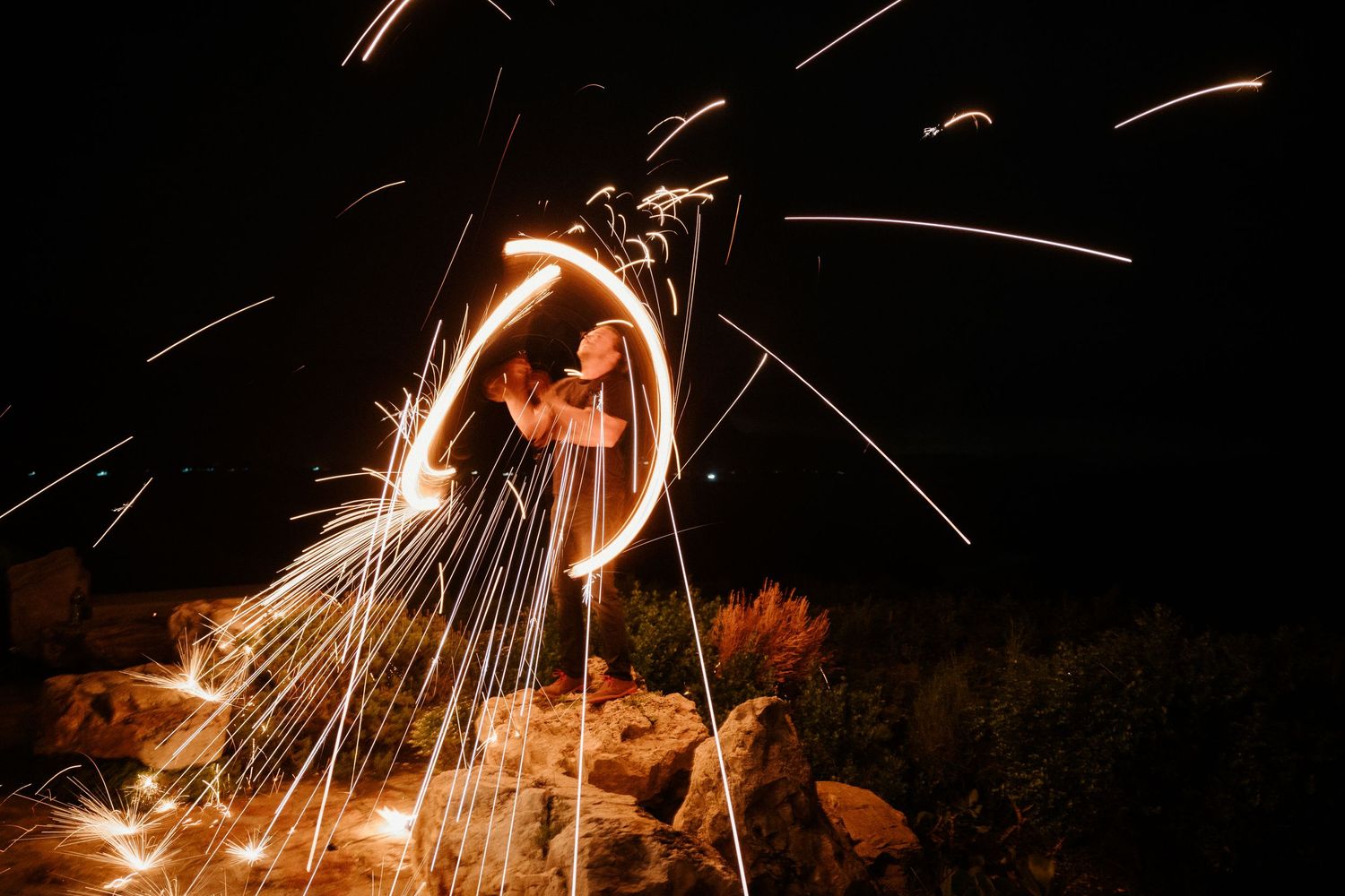 Spectacular steel wool fire spinning performance creating trails of light against night sky.