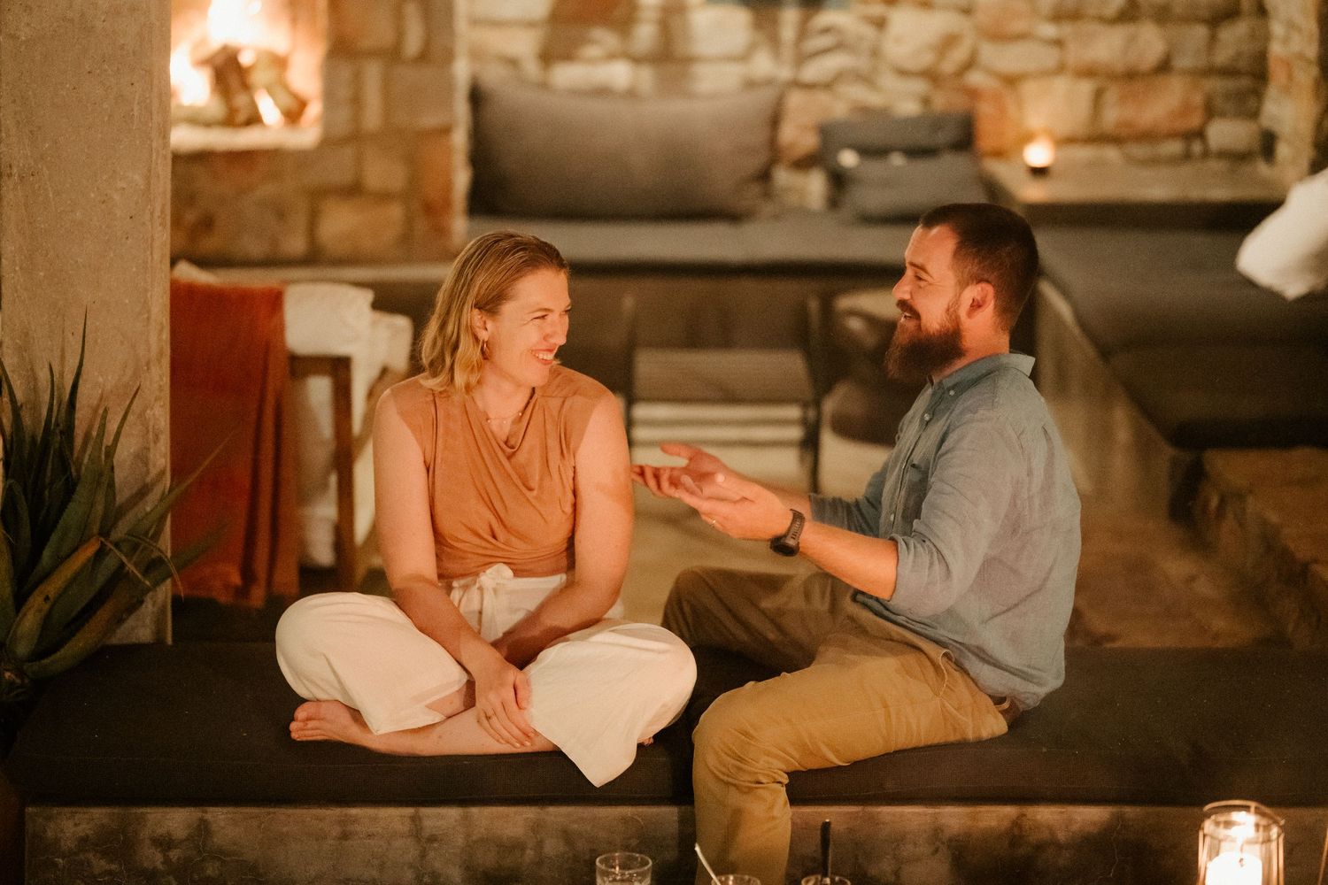 Two people having intimate conversation in rustic indoor setting with warm lighting.