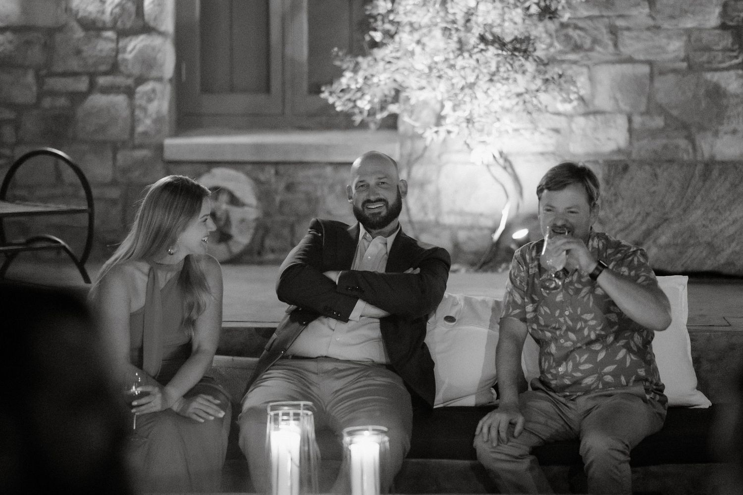 A candlelit evening gathering with guests sharing laughs on outdoor seating.