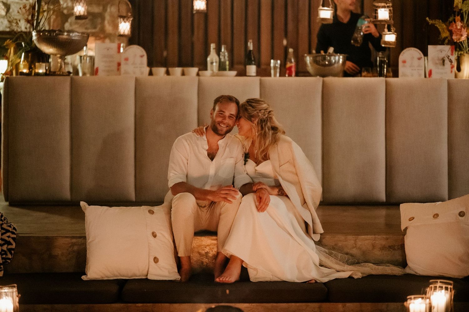 A couple sits together on cushions surrounded by romantic candlelight at an evening reception.