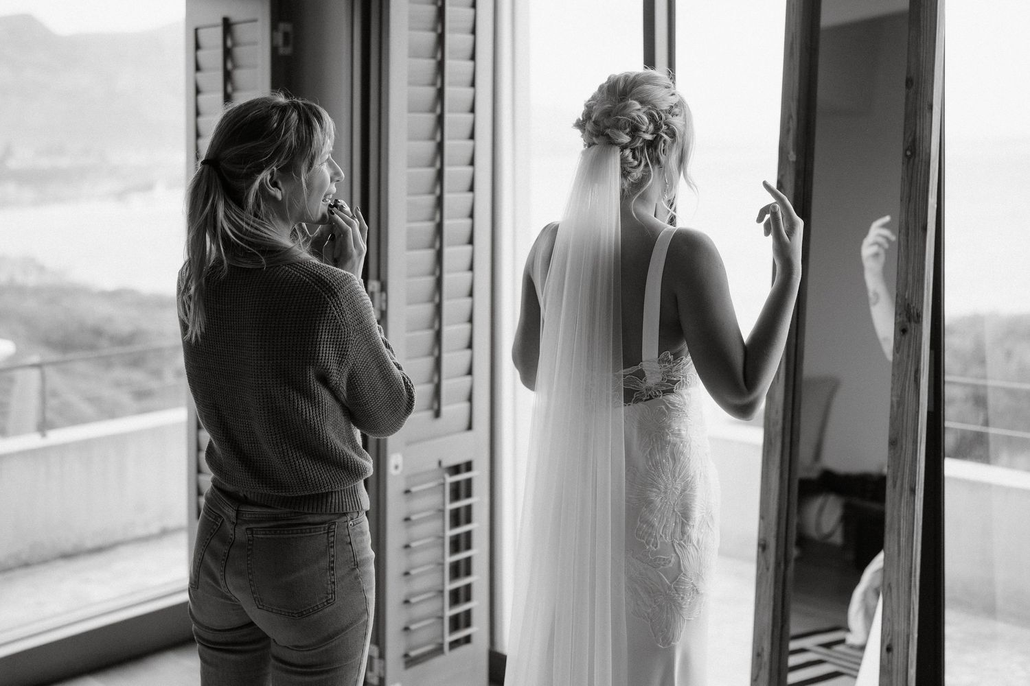 Two figures silhouetted against bright windows during wedding preparation.