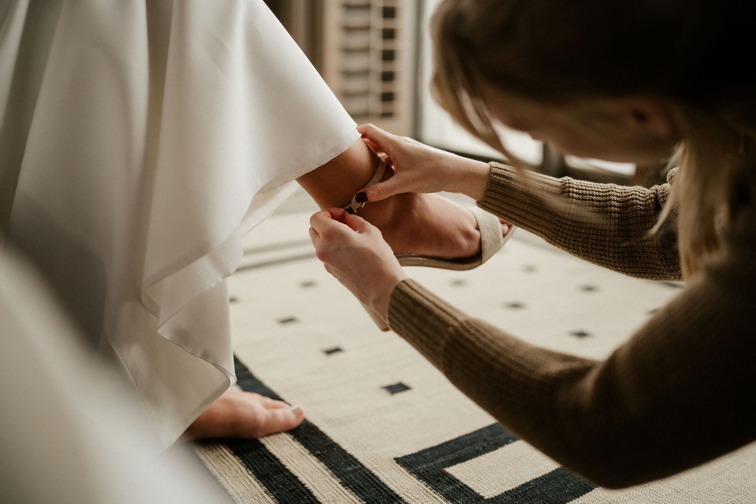 Close-up shot of hands measuring and marking on white fabric during a wedding dress fitting session.