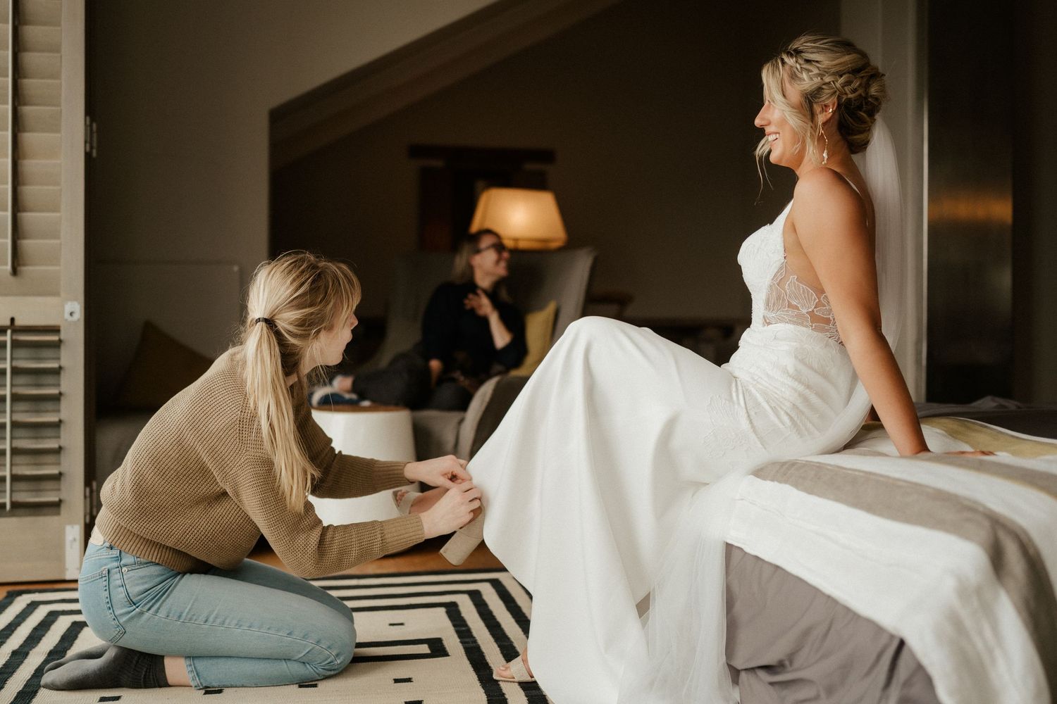 A wedding dress is carefully adjusted before the ceremony in an elegantly furnished room.