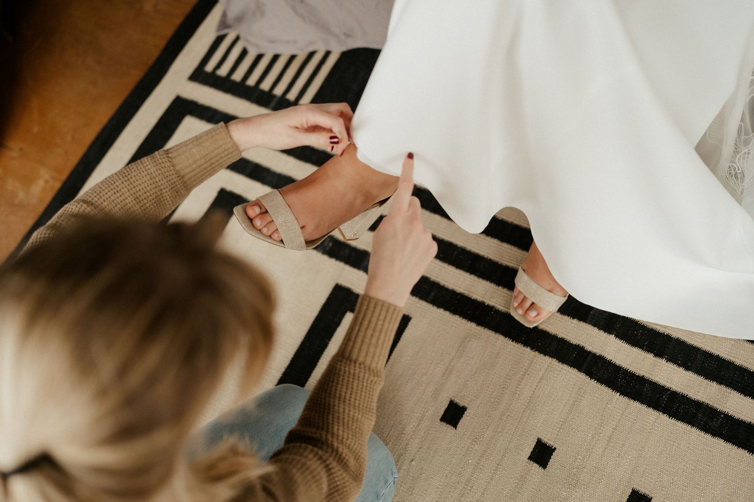 Close-up of blush pink heeled sandals on a black and white striped rug.