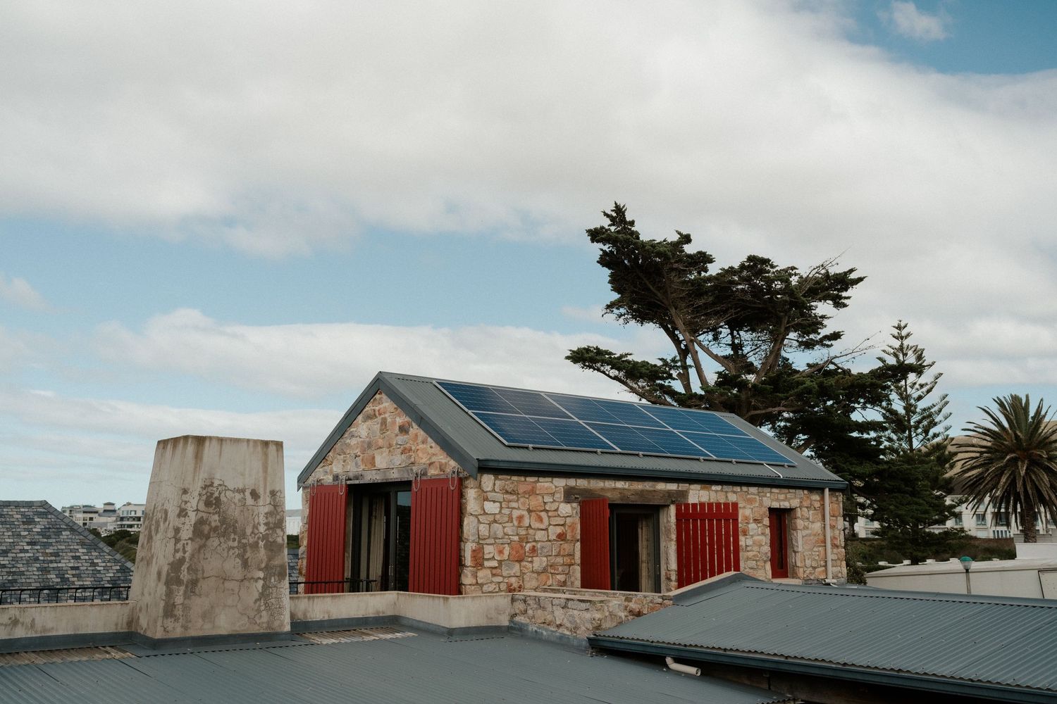 A stone building with red accents and solar panels on the roof under cloudy skies.