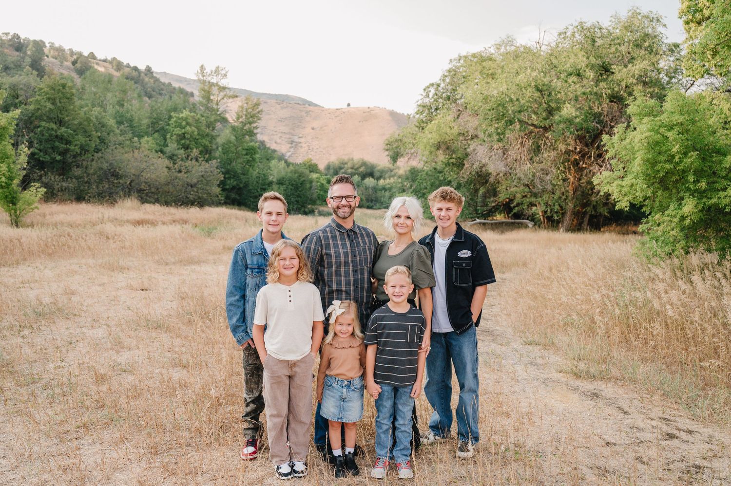 A group of people standing together in a grassy field during golden hour with hills in the background.