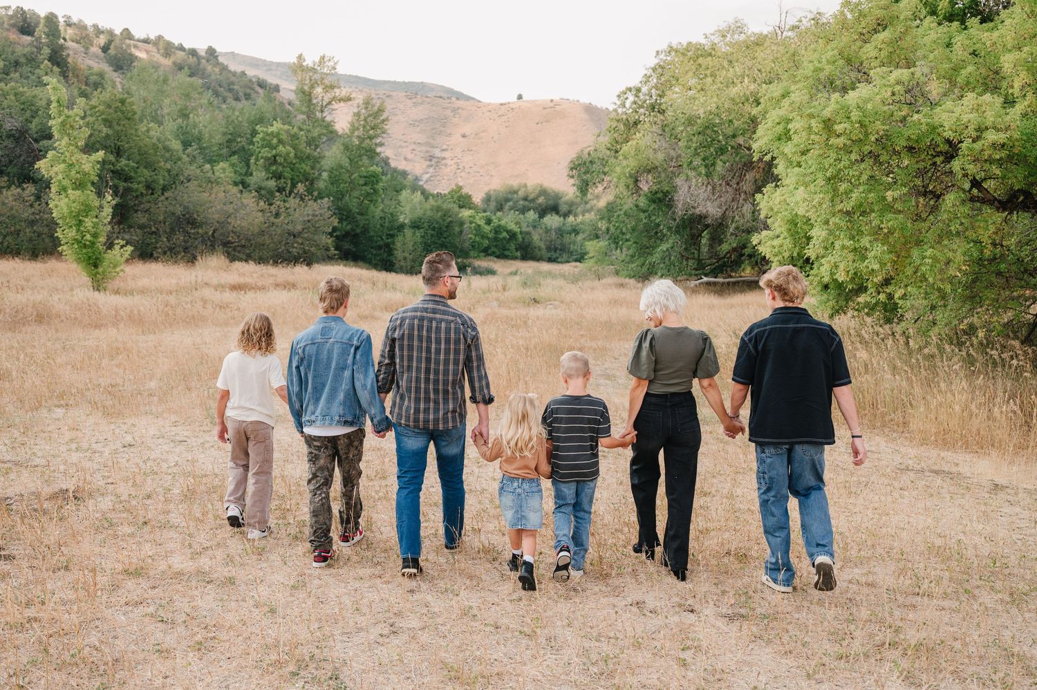 A group of people walking together on a dirt path through golden hills on a sunny afternoon.