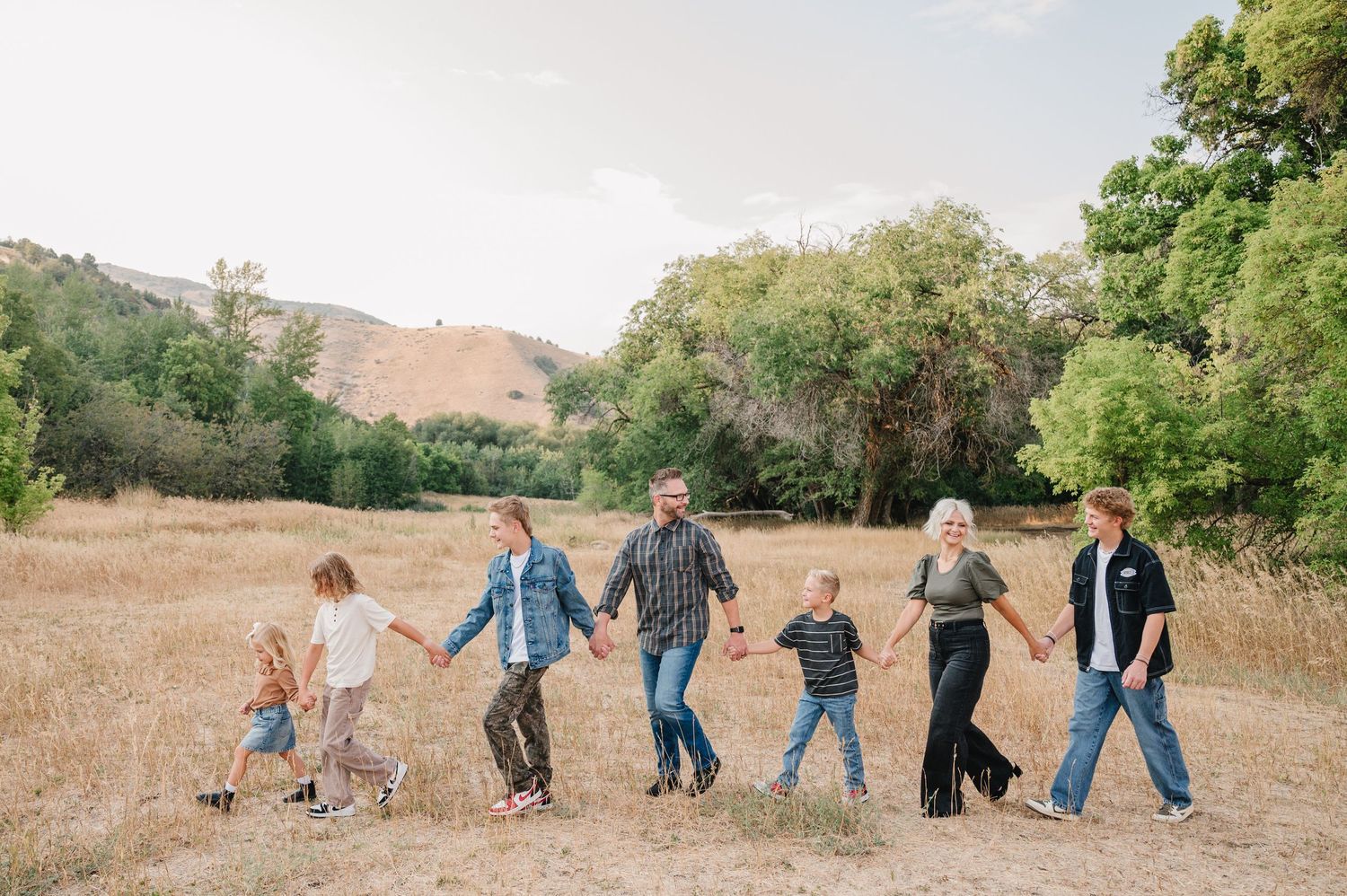 A panoramic sequence of people falling over in a grassy field during a playful outdoor photo shoot.