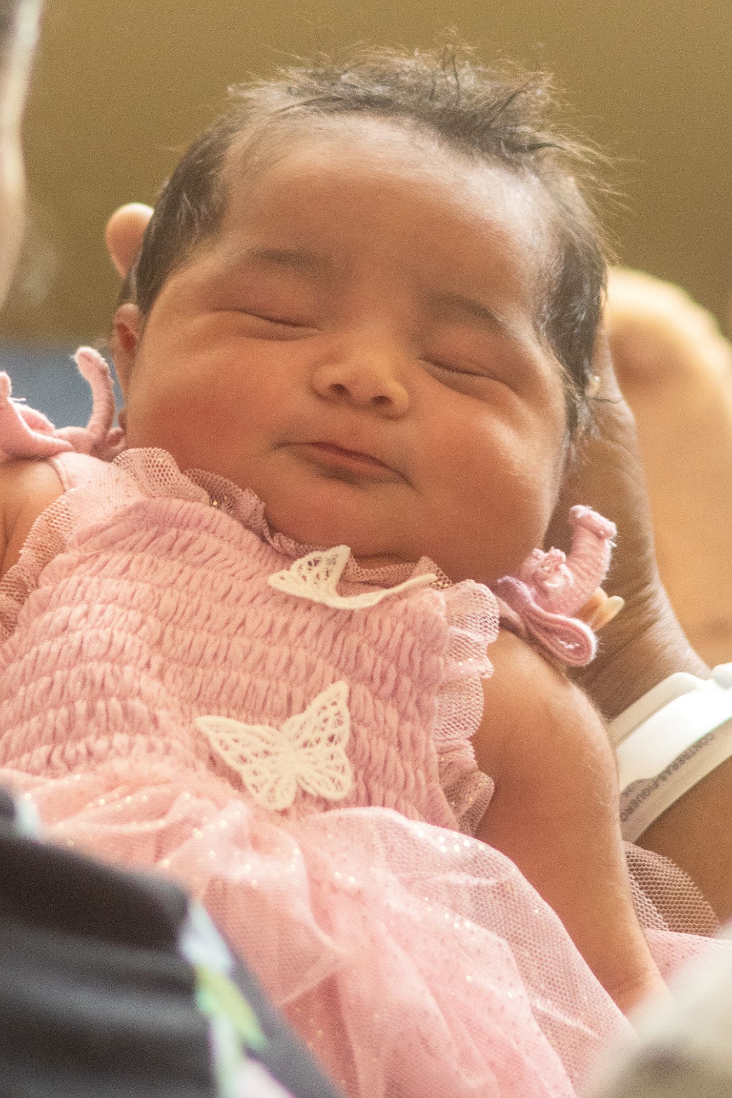 A sleeping baby wearing a pink smocked dress with delicate lace details.