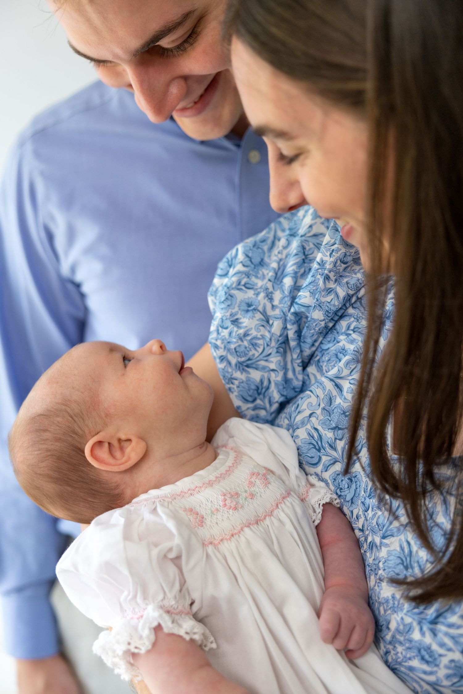 Happy parents smiling at their newborn baby dressed in white, sharing a tender family moment.