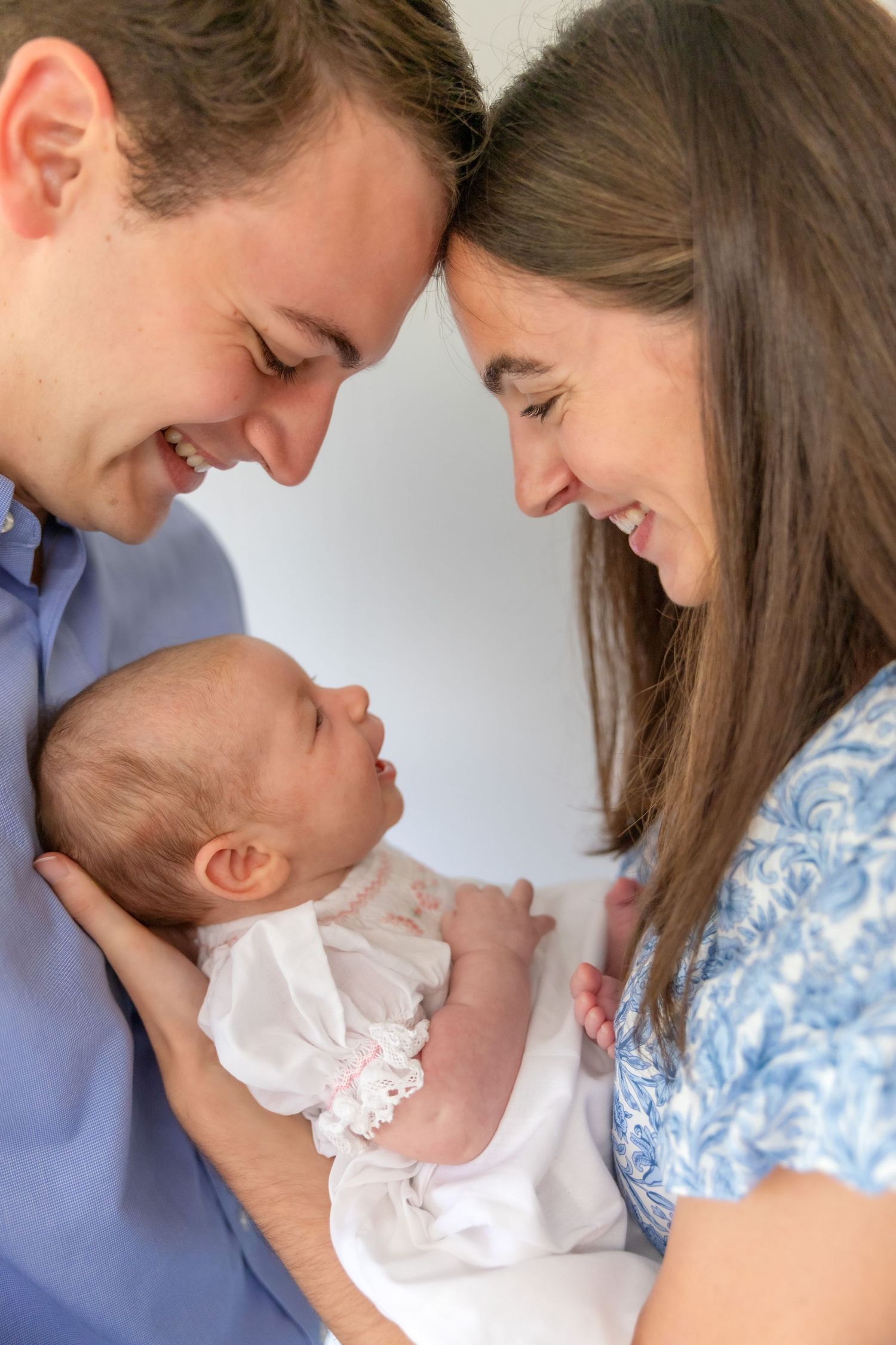 Happy parents smiling at their newborn baby, with foreheads touching in a tender family portrait.