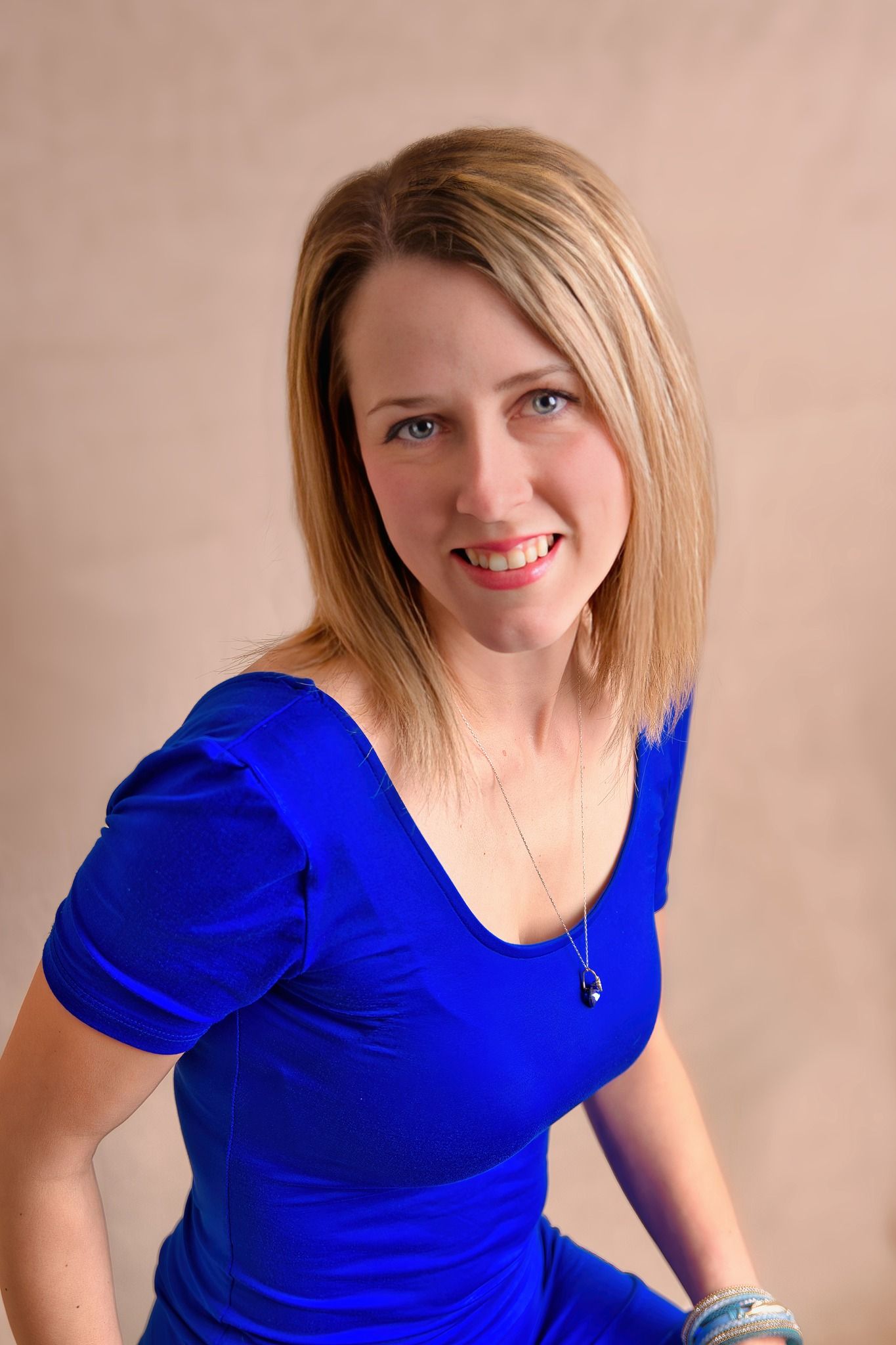 Professional portrait of a person wearing a vibrant royal blue top with a delicate necklace against a neutral background.