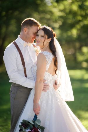 A romantic wedding couple embraces in a sunlit garden setting with beautiful natural lighting and greenery.