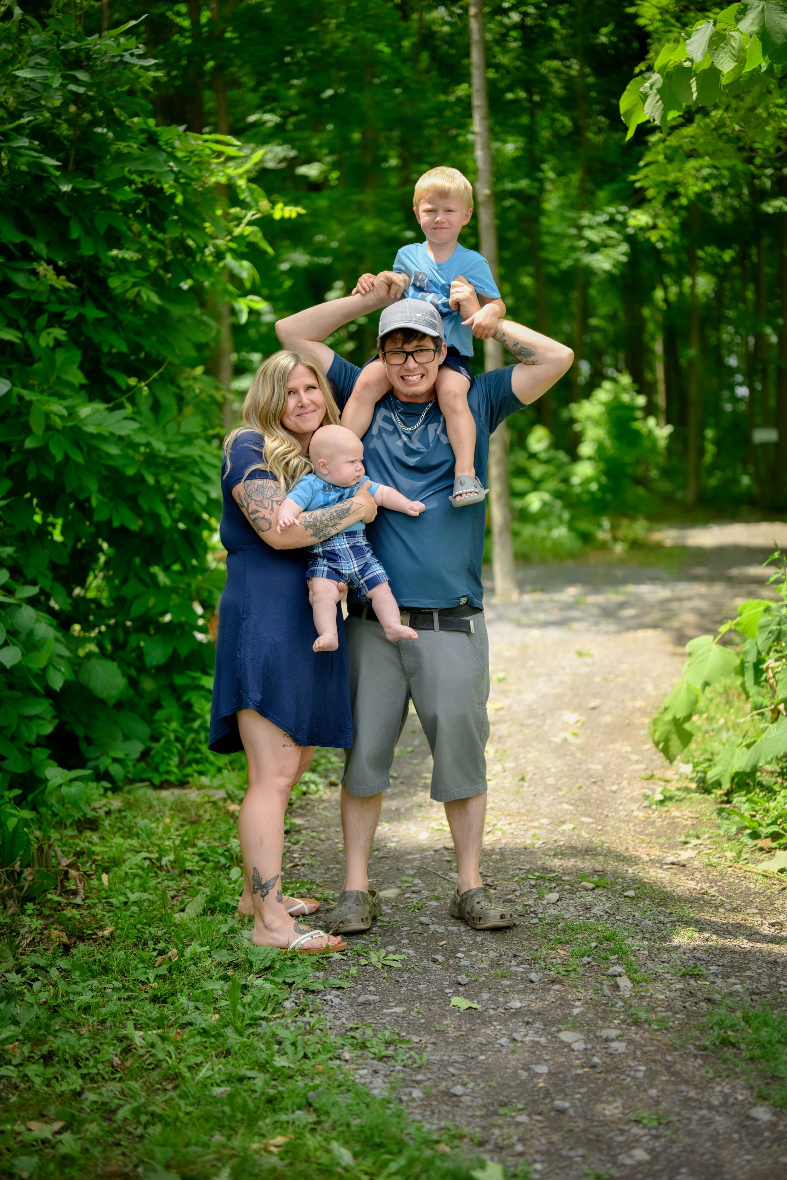 A family enjoys a summer hike together on a wooded trail surrounded by lush green foliage.