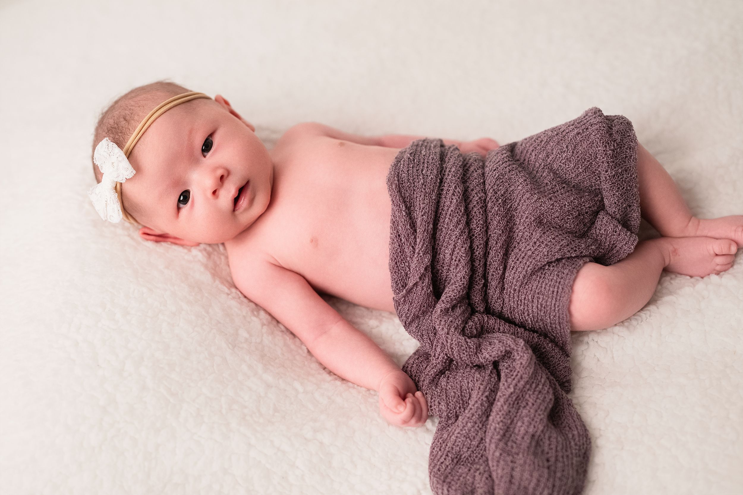 Four newborn babies wearing brown knit wraps lie side by side on a white background.
