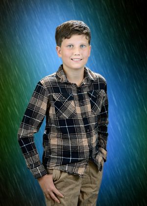 A child wearing a plaid button-down shirt and khaki pants poses against a blue-green gradient studio backdrop.