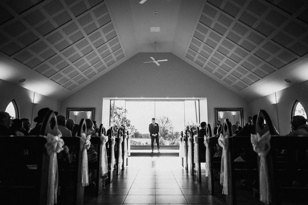 Black and white image of a long empty corridor with a vaulted ceiling and fluorescent lighting.