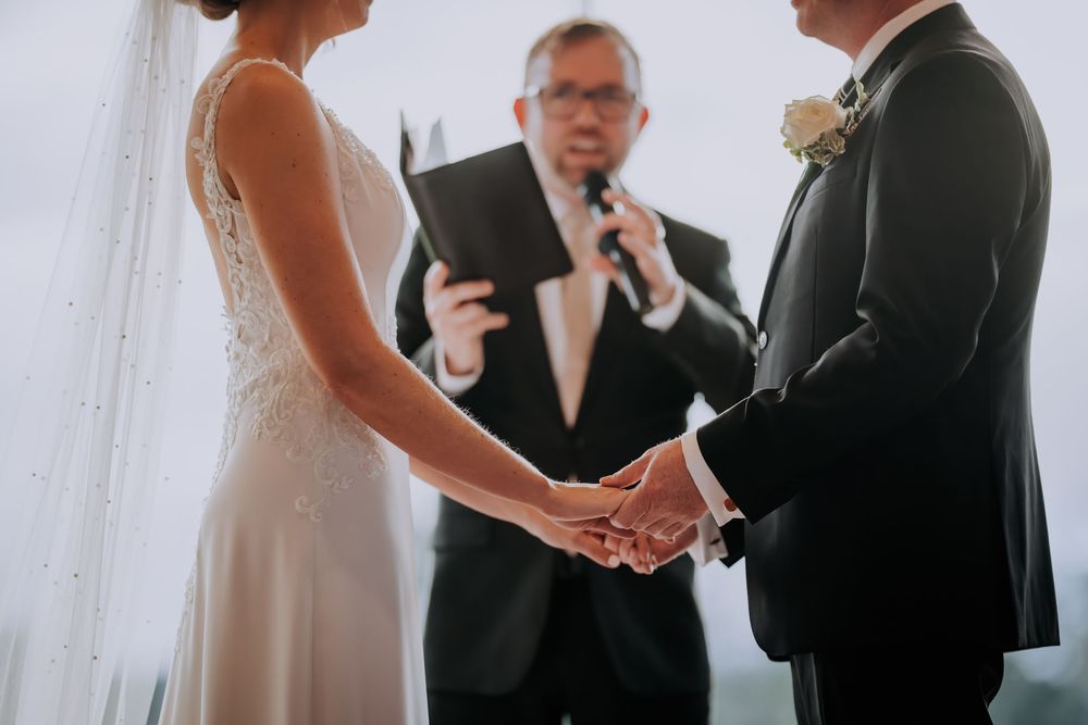 A couple exchanges vows during an intimate wedding ceremony with a white curtain backdrop.
